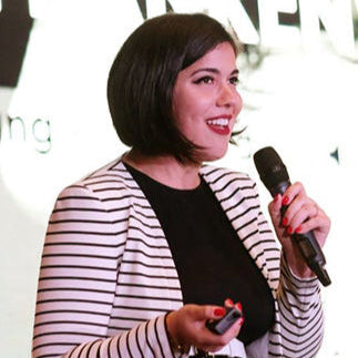 Woman holding a microphone and remote control in front of a blurred background with text.